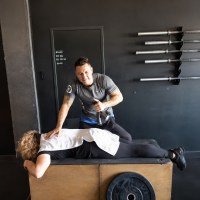 Entrenador personal utilizando una pistola de masaje para favorecer la recuperación muscular y aliviar la tensión después del ejercicio.